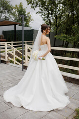 Elegant bride in a beautiful gown standing outdoors with flowers on a cloudy day