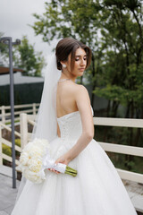 Bride in elegant white gown holds bouquet while looking back at outdoor venue in serene moment