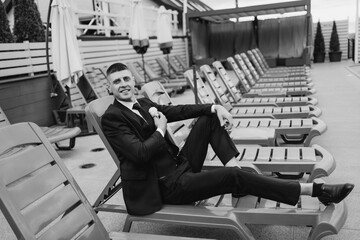 Groom relaxes by a pool on his wedding day with a stylish suit and confident smile
