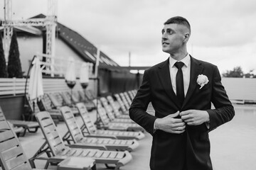 Groom adjusting tie at a poolside venue during wedding preparations in overcast weather
