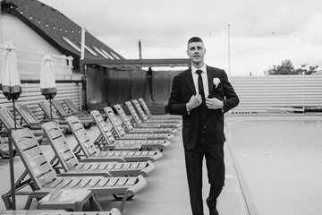 Groom adjusts suit while walking by poolside area during wedding celebration