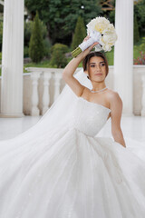 Bride in stunning white gown poses elegantly with bouquet at outdoor venue during golden hour
