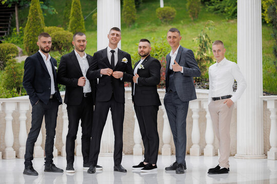 Groom and groomsmen pose together in formal attire at outdoor venue before wedding ceremony