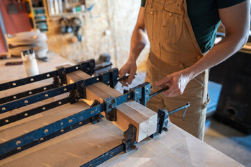 Carpenter hands using clamps to press wooden beams together applying glue for large board assembly...