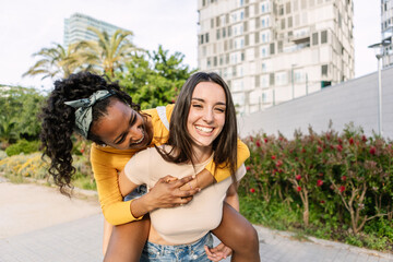 Portrait of two female friends are enjoying a playful moment in a city park, with one giving the...