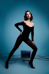 Graceful brunette woman posing in black bodysuit and tights during a studio vertical photoshoot...