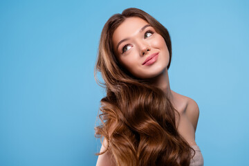 Portrait of a young woman with long wavy brown hair and healthy skin in a studio with a blue...