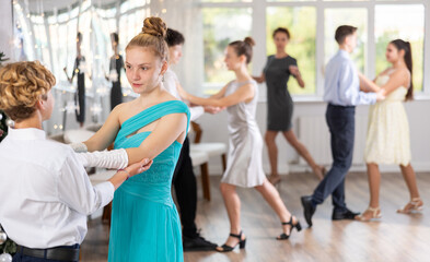 Positive teen boy and girl are dancing classic version of waltz in couple during lesson at studio...