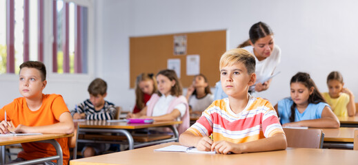 Portrait of diligent schoolboy who writing exercises at lesson in primary school