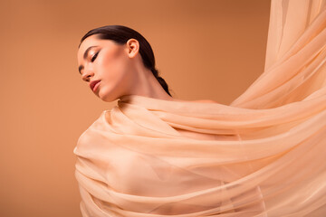 Elegant portrait of a young woman wrapped in flowing beige fabric, showcasing beauty and grace