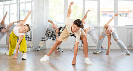 Naklejka premium Positive teenage boy practicing hip-hop dance in training hall during group dancing classes