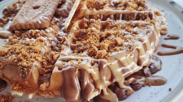 Waffle dessert topped with Biscoff spread, chocolate drizzle, cookie crumbs, and biscuit