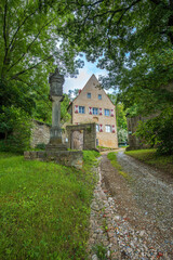 Historic building with half-timbered charm, surrounded by forest and nature, reached via an old cobblestone path with a stone gate and monument