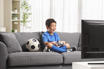 Boy sitting on a sofa with a football and playing a video game