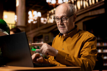 Elderly wise college student interacting with professor at webinar on laptop, studying in a library...