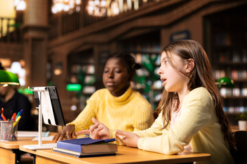 Diverse schoolgirls at a study table attending virtual webinar class, focusing on e learning and...