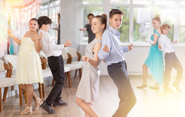 Group of positive teenagers, girls and boys, rehearsing jazz-style routine in dance studio....