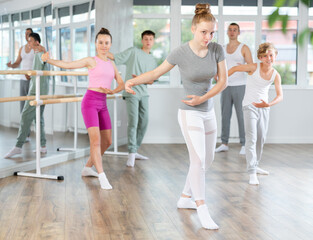 Gracious teen girl doing choreography in group with instructor during ballet classes in dance studio
