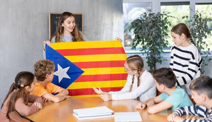 Geography lesson in school class - teacher talks about Catalonia, holding a flag in his hands
