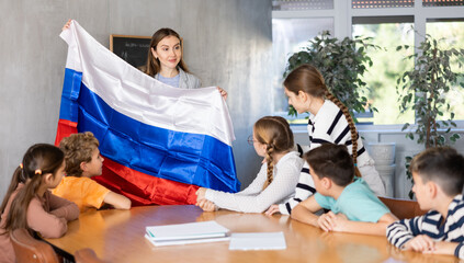 Pupils having lesson of geography. Female teacher discussing with children about national flag of...