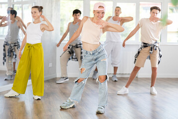 Girl in baseball cap with two hair pigtails with group of teenage friends, learn to dance hip hop...