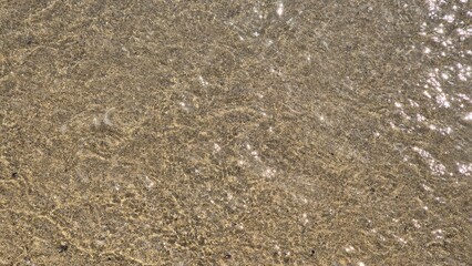 Seawater gently moves over sandy ground at Matosinhos beach, Portugal, on a sunny day, capturing natural textures, light reflection, and coastal motion.