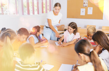 Positive young female teacher giving lesson for group of preteen schoolchildren sitting around...