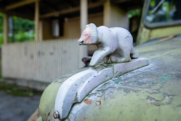 Close-up of weathered bear hood ornament on vintage truck, rusty car hood with retro bear figurine...