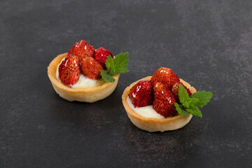 Two Mini round tartlets with strawberries and mint. Dark background. Close up	