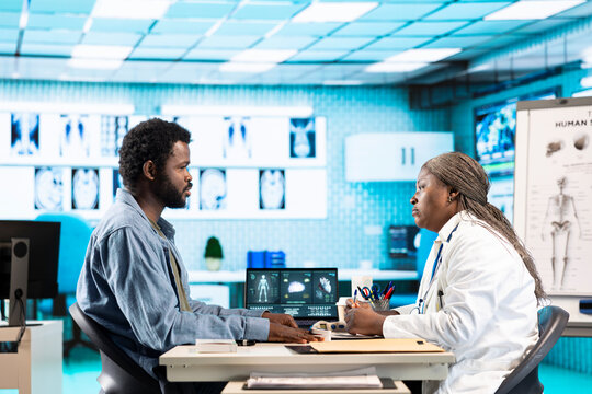 Medic expert checking oxygen saturation and pulse rate using oximeter during routine checkup, consulting her male patient with modern medical equipment. Vital signs measurement.