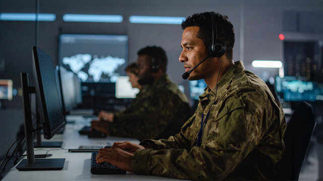 Soldiers working diligently at their stations inside a command center. The image highlights their focused concentration while they operate advanced technological equipment.