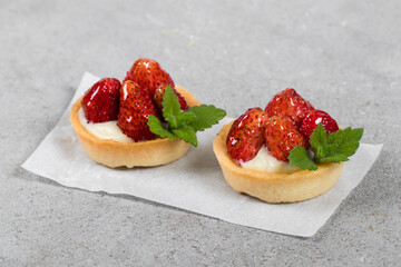 Two Mini round tartlets with strawberries, custard and mint.  Light gray background. Close up
