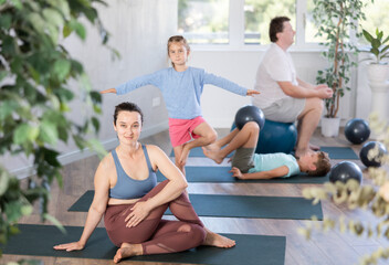 Obraz premium Family with two children doing yoga with softball on mats in fitness studio