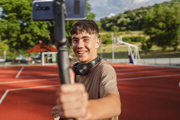 teenage boy with skateboard filming video with mobile phone on court