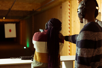 Shooting range instructor ensuring safety protocols are followed while woman uses pistol to hit...