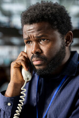 Black corporate employee engages in a landline phone call at the office, managing a project...