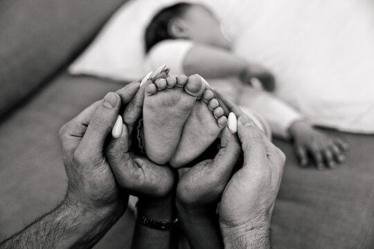 Father and mother holding baby feet - Family and newborn concept with mom and dad staying with daughter at home - Black and white filter