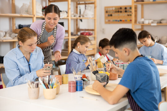 Positive children engaged in working with clay handmade items in workshop together with teacher