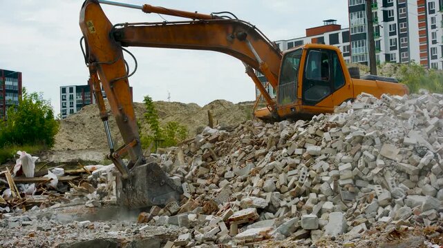 Excavator with bucket works on construction site. Loading machine dismantles pile of broken bricks and concrete left after demolition of old house. Tracked excavator digs with hydraulic bucket, shovel