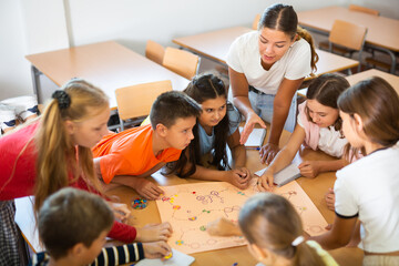 Schoolkids playing interesting board game with teacher in classroom. Boys and girls playing...