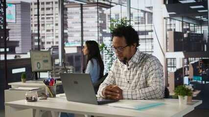 Black man employee joins a telecommuting session at his office desk, multitasking between project...