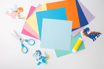 Paper cutouts of fairy and paper dinosaurs with glue stick, scissors, and multicolored paper sheets...