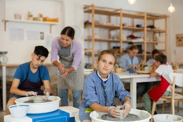 Interested girl sculpts with her own hands from white clay on a potter's wheel in a creative...
