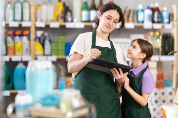 Woman seller with daughter, make inventory using tablet in store. Little girl helps her mother...