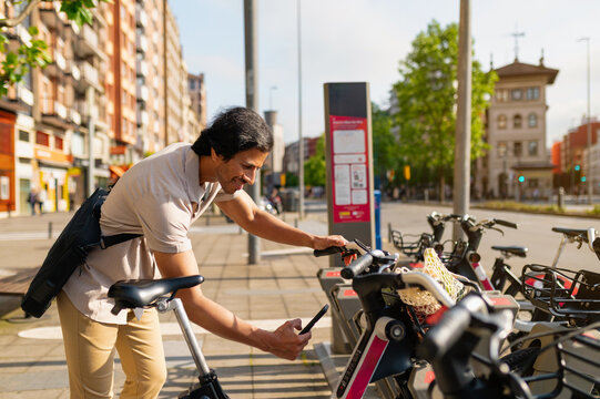 Young businessman renting an electric bicycle in the city using a smartphone app for urban mobility and sustainable commuting