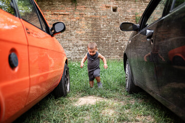 Toddler walking between two parked cars near brick wall