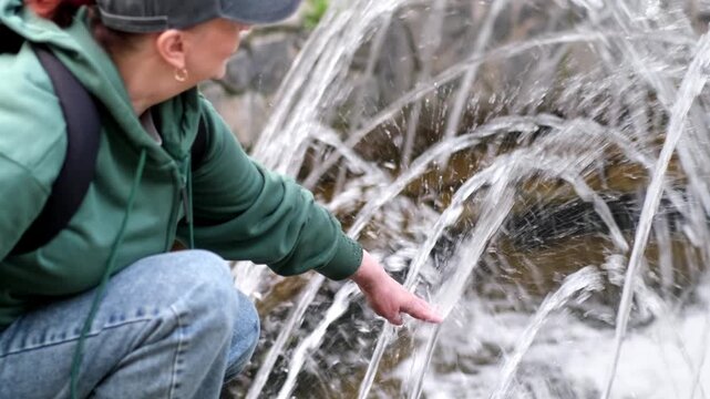 Woman playing with water from a fountain in a city park. 4k video
