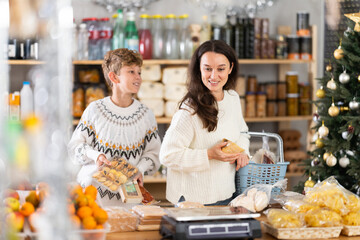 Teen boy and mother looking at snacks in store. Market visitors choose consider nougat, panettone,...