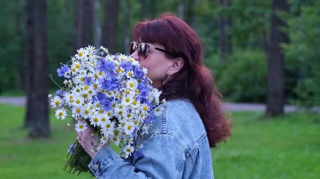 A woman holds a gift in her hands - a huge bouquet of wild flowers. daisies and cornflowers. Video 4k.