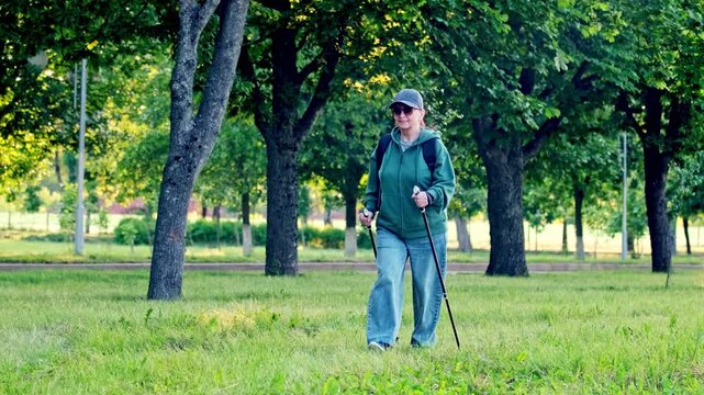 Active woman doing Nordic walking in city park, sporty outfit, using walking poles, healthy lifestyle and outdoor exercise, 4K UHD stock footage.